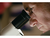A close up photo of Carl June looking into a microscope.